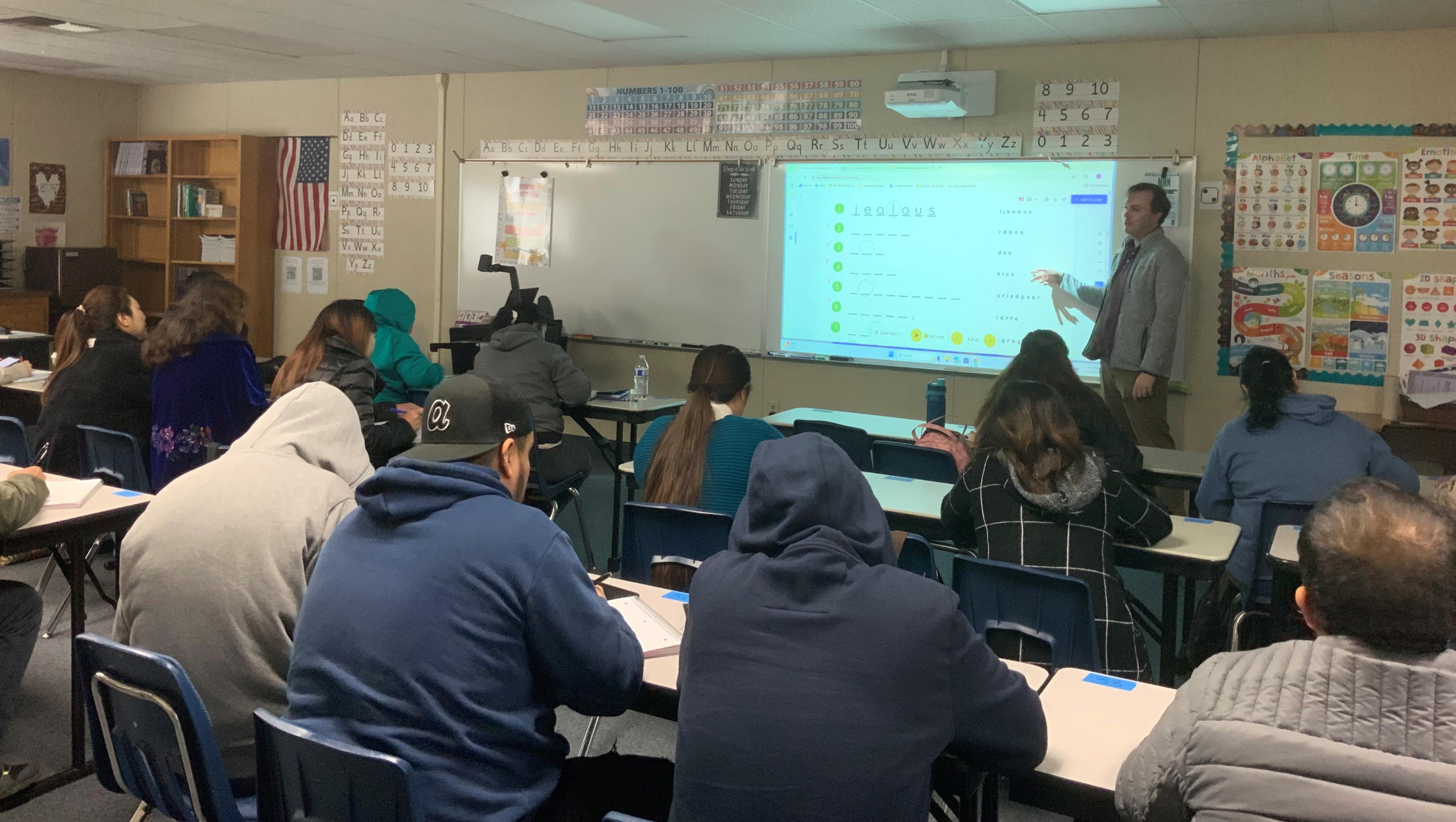 Instructor in front of a class full of students pointing at the white board assignment.